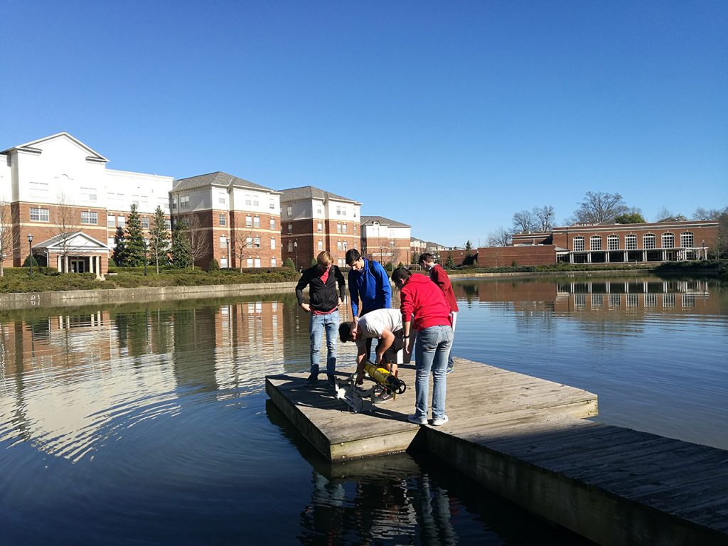 Students standing on a pier in the middle of a lake.