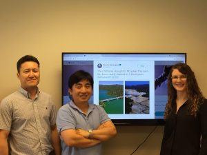 Three people standing in front of a monitor.