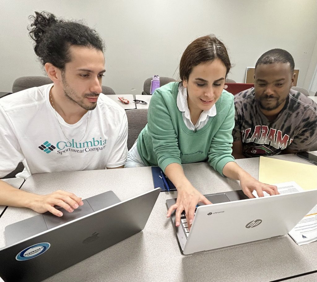 Two students and a mentor reviewing water science data sitting at a table with two laptops.