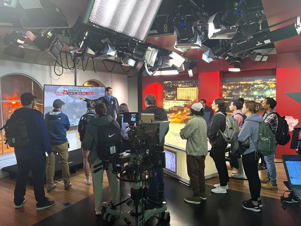Students and researchers standing behind-the-scenes in a TV studio while on air.