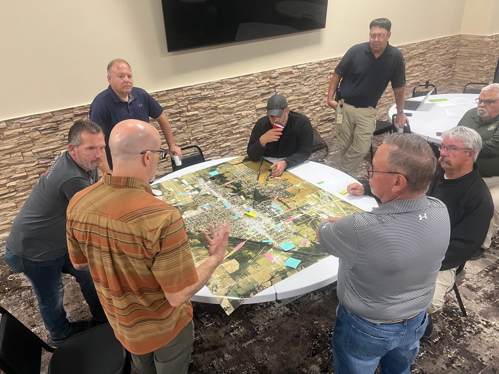 Emergency managers and local leaders gather around a large map, discussing potential flooding areas of concern.