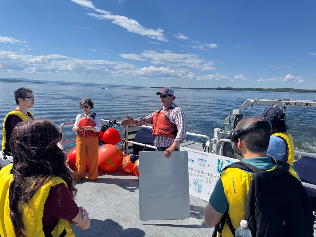 A group of six people in lifejackets on a boat, with open water visible behind them.