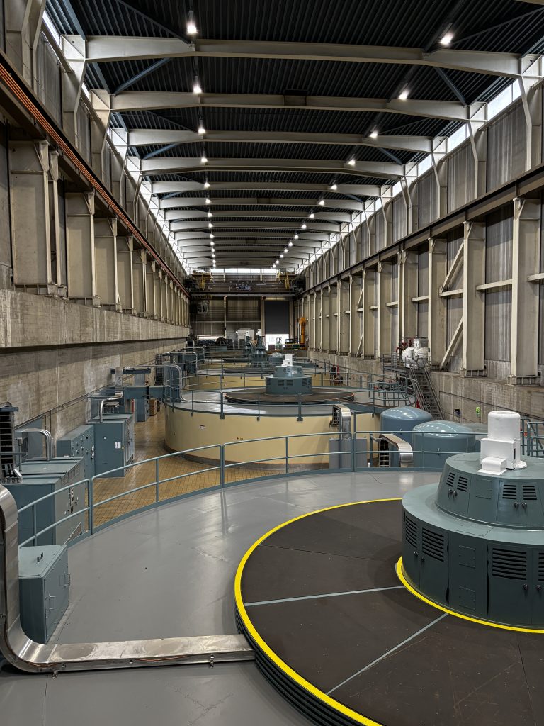 Rows of large circular generators are lined up inside a dam power station.