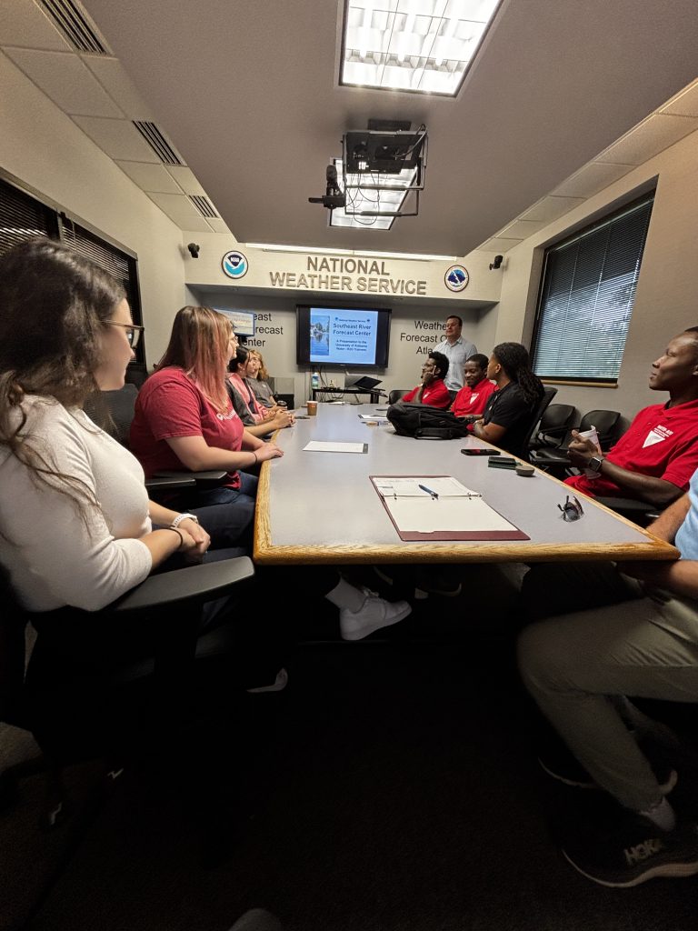 People sit around a conference table at the National Weather Service while a presenter speaks.