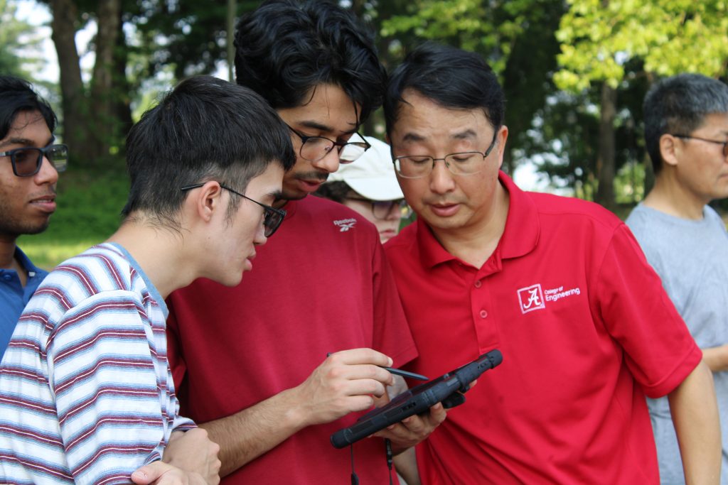 A faculty member from The University of Alabama’s College of Engineering reviews data on a tablet with two students during a field activity.