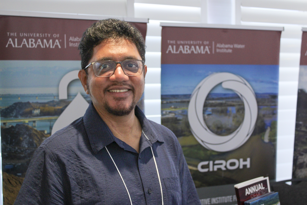 A man stands smiling in front of Alabama Water Institute and CIROH banners at The University of Alabama.