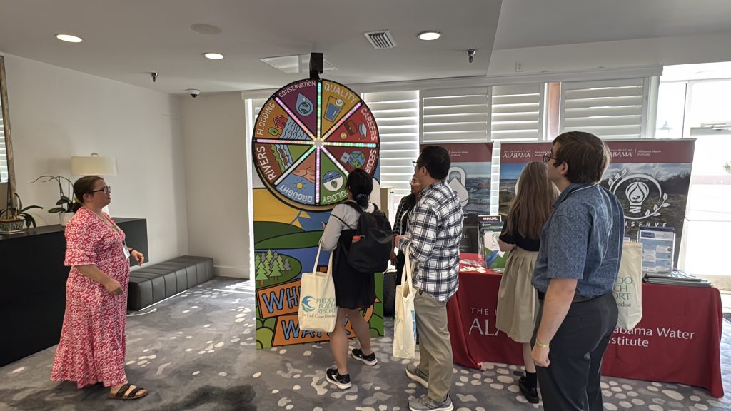 Conference attendees visiting the Alabama Water Institute table and spinning the Wheel of Water.