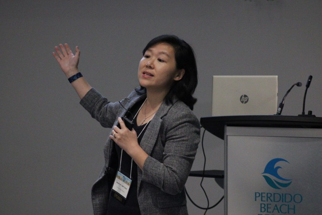 Person gesturing while delivering a conference presentation.