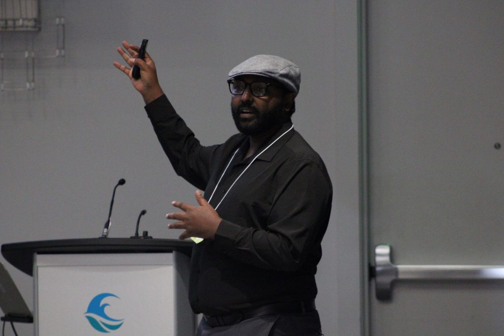Person gesturing while delivering a conference presentation.