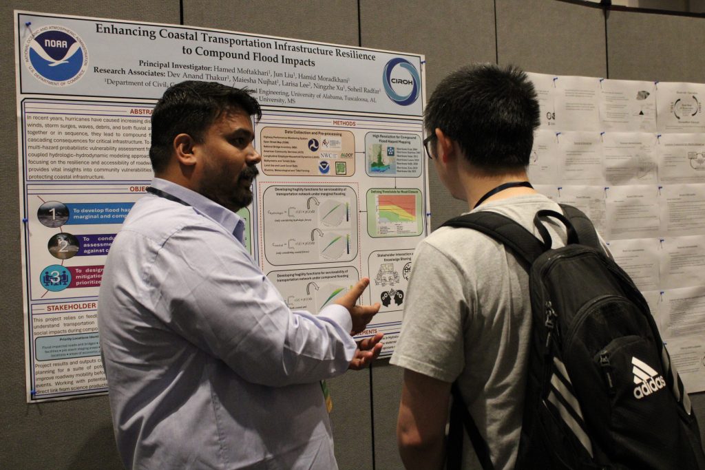 People in a conference hall gathered in front of research posters and engaged in discussion.