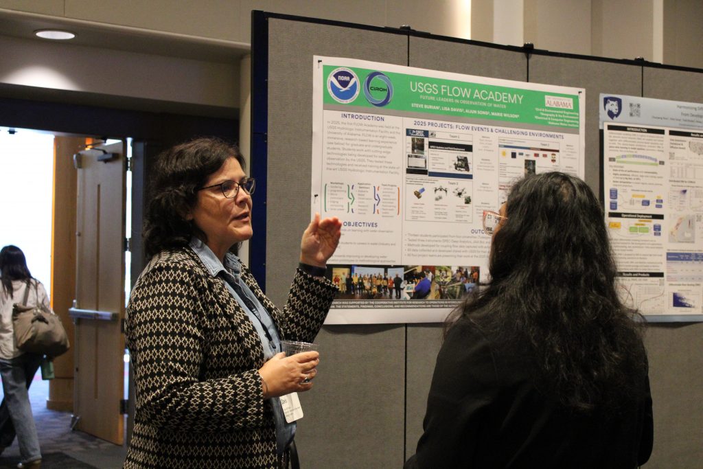 People in a conference hall gathered in front of research posters and engaged in discussion.
