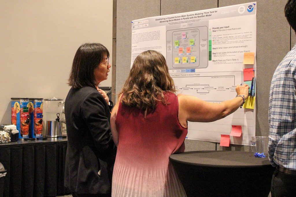People in a conference hall gathered in front of research posters and engaged in discussion.