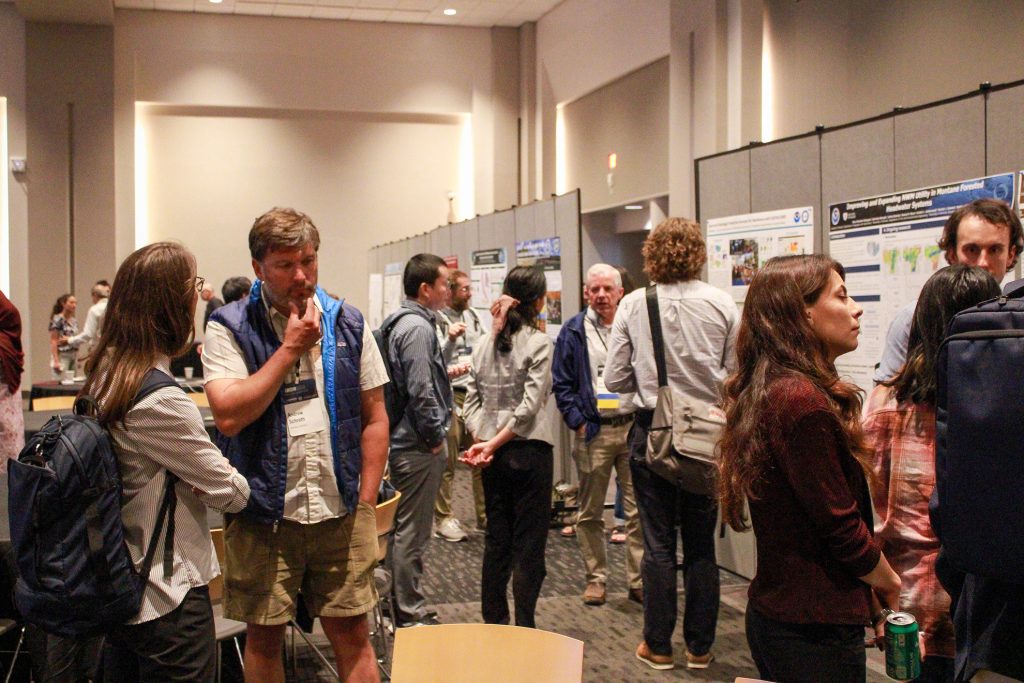 People in a conference hall gathered in front of research posters and engaged in discussion.
