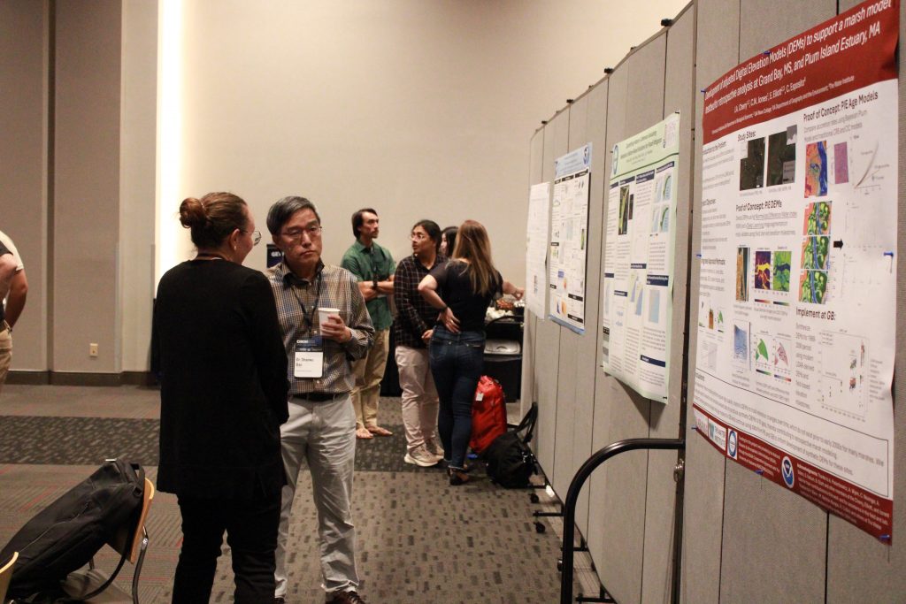 People in a conference hall gathered in front of research posters and engaged in discussion.