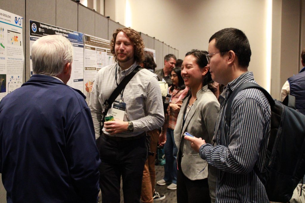 People in a conference hall gathered in front of research posters and engaged in discussion.