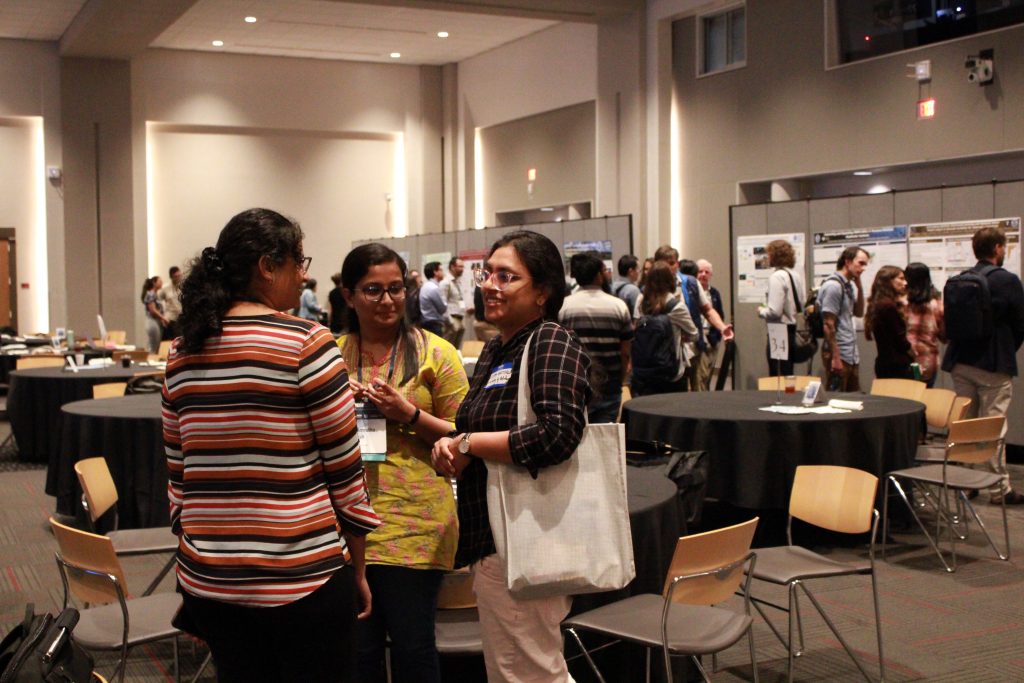 People in a conference hall gathered in front of research posters and engaged in discussion.