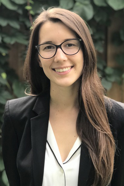 Person with brown hair, white shirt, and black coat standing outside.