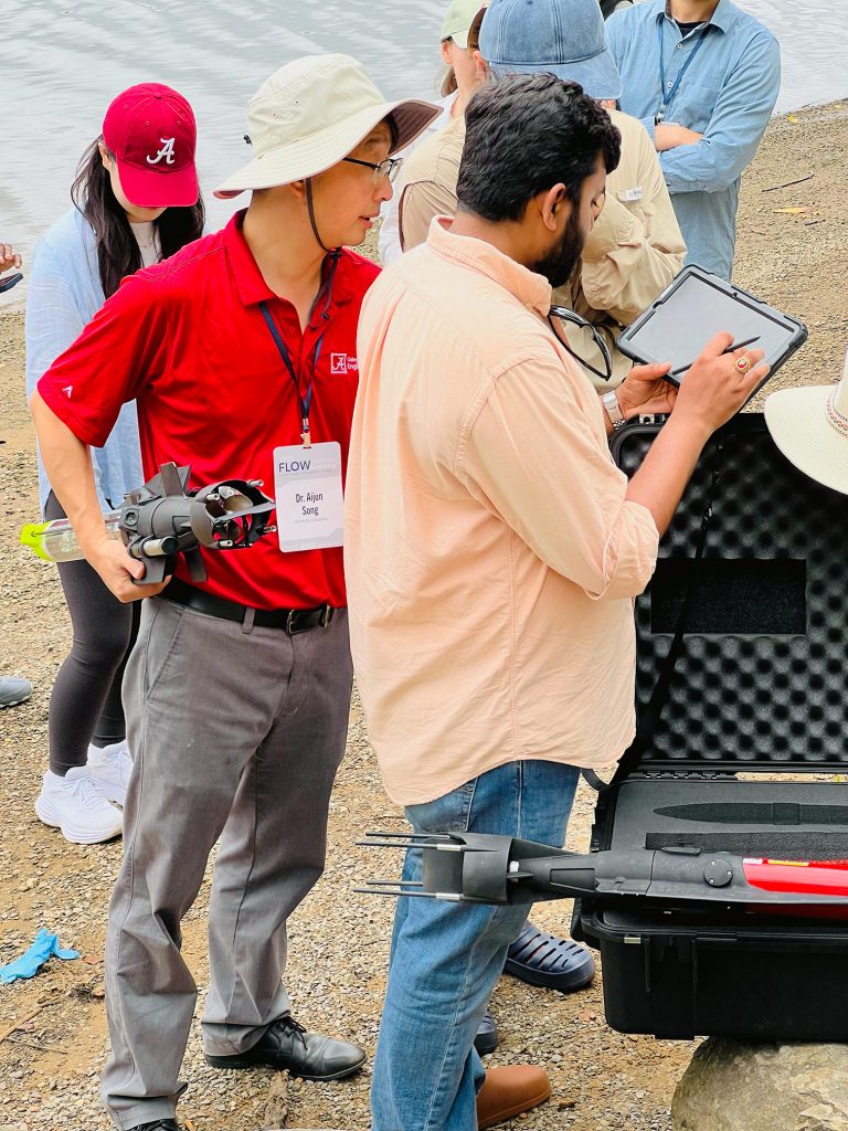 Field work with Dr. Song, UA FLOW Academy students standing on the bank of the Black Warrior River deploying AUVs.