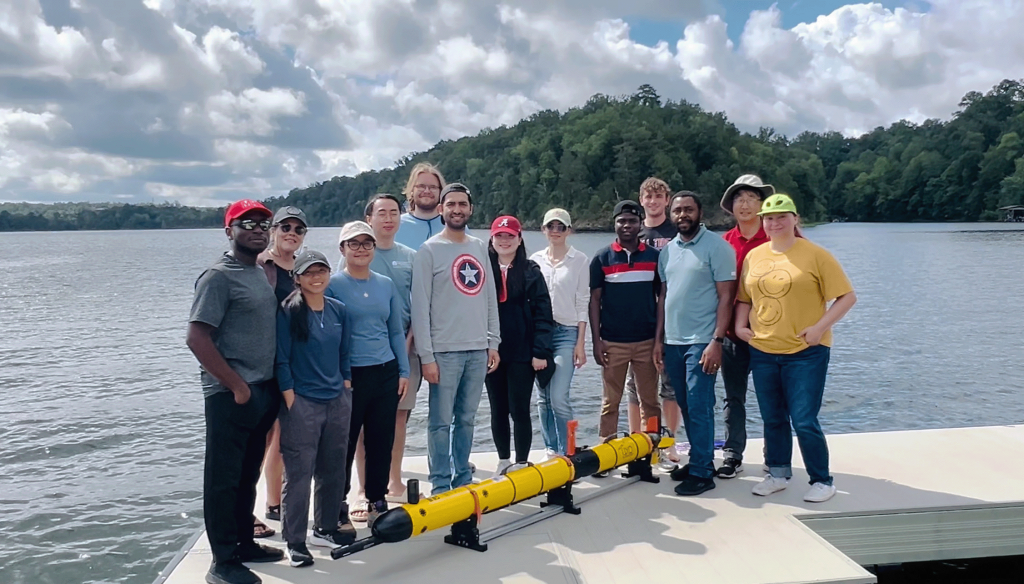 Group photo of all 13 UA FLOW Academy students on the dock at Sharpes Landing holding AUV with mentors Dr. Davis and Dr. Song
