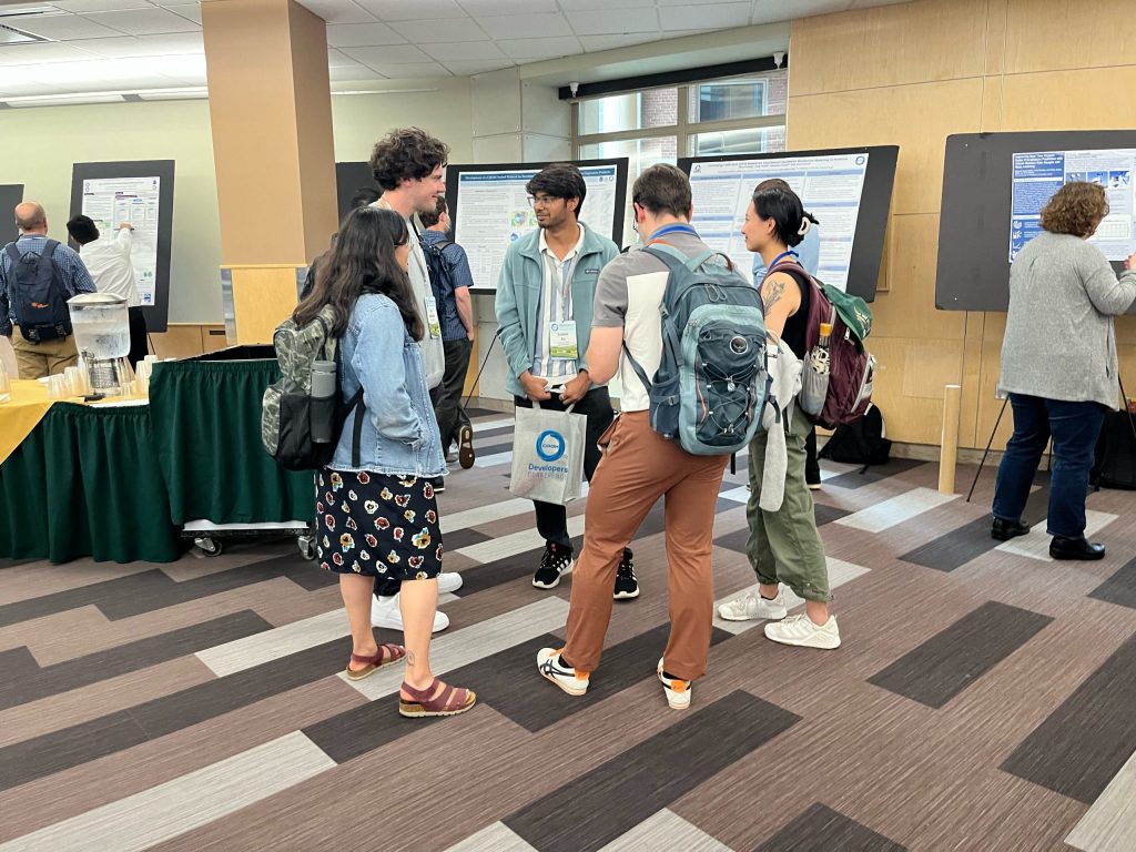 A group of five people chatting in a circle with poster presentations going on behind them.