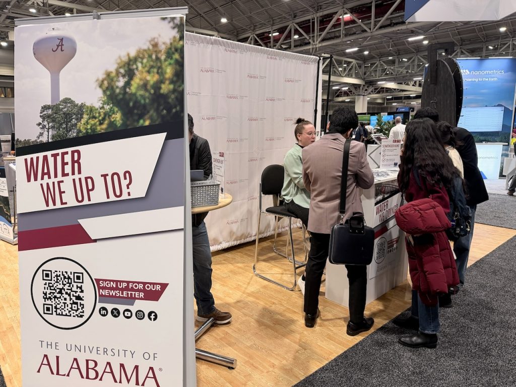 An AWI banner stands at the booth as attendees gather around the table in discussion.