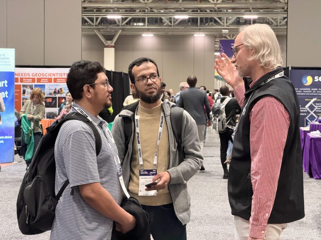 Attendees discuss scientific topics in the AGU25 convention hall near the CIROH exhibit area.