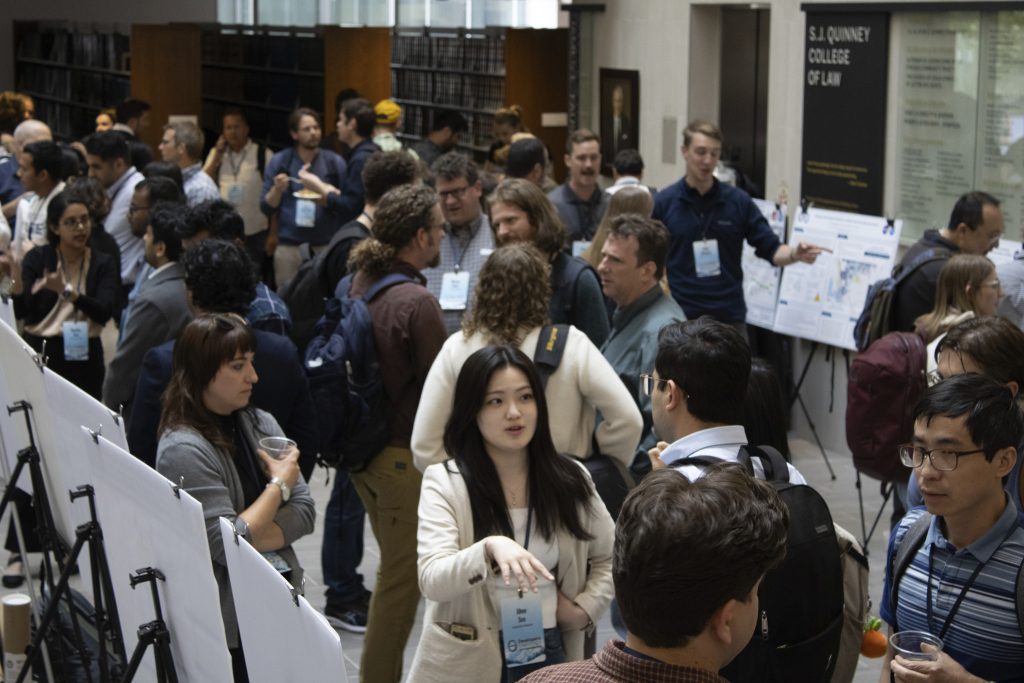 Photograph showing a group of people engaged in conversation around academic posters. 