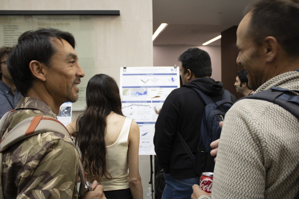 Photograph of a group of people standing and viewing a scientific poster presentation in an indoor setting.